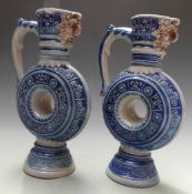 A pair of German Mettlach style mask spouted pedestal ewers of circular form, H20cm