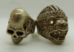 Two oriental style white metal rings, one in the form of a dragon mask, the other as a skull,
