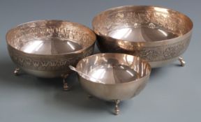 Set of three graduated white metal bowls with embossed decoration, raised on three feet and marked