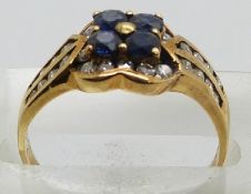 A yellow metal ring set with four round cut sapphires and diamonds in a flower cluster, 3.3g, size