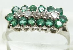 A 9ct white gold ring set with a row of diamonds surrounded by emeralds, 2.1g, size L