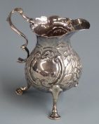 Georgian hallmarked silver cream jug with embossed decoration and raised on three feet, London