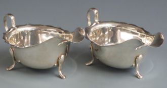 Pair of hallmarked silver sauce boats with shaped edges, raised on three feet, Sheffield 1953 and
