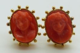 A pair of yellow metal earrings set with carved coral cameos within a sphere border