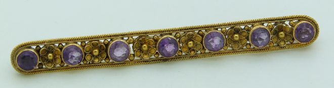 A yellow metal early 20thC brooch set with alternating amethysts and gold flowers, 4.4g, 6.2cm long