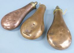Three copper and brass powder flasks one stamped 'Patent', largest 19.5cm long.