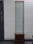 A glazed cabinet with three glass shelves raised on a wooden base with lockable storage compartment,