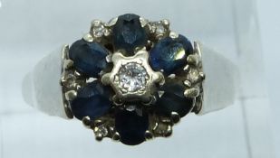 A 9ct white gold ring set with a diamond to the centre surrounded by sapphires, 3.6g, size Q