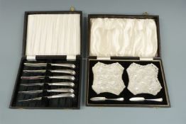 Cased pair of cut glass butter dishes with hallmarked silver knives together with a cased set of six
