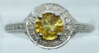 An 18k white gold ring set with a round cut yellow sapphire surrounded by diamonds with further