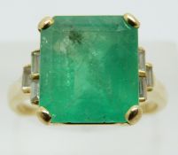 An 18ct gold ring set with a natural emerald cut emerald of approximately 5.97cts and three baguette