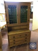 A blonde oak double door leaded glass door bookcase fitted with three drawers beneath