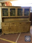 A blonde oak four door kitchen dresser fitted with cupboards and drawers beneath