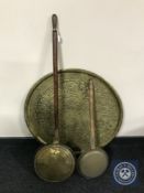 A circular Eastern brass embossed wall plaque and two bed warming pans