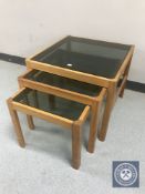 A nest of three mid twentieth century teak smoked glass topped tables
