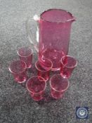 A cranberry glass water jug and six small beakers