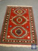 A Persian fringed rug on red ground,