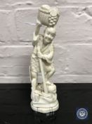 A Japanese carved bone okimono in the form of a street vendor holding a basket of fruit,