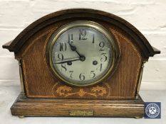 An inlaid oak cased mantel clock with brass column supports, enamelled dial,