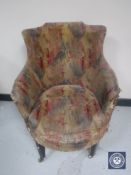A Victorian armchair upholstered in a multi-coloured fabric raised on brass castors