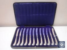 A set of twelve silver handled pistol grip butter knives, cased.
