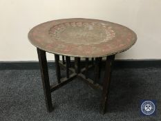An Eastern brass topped table on folding oak base