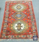 A Caucasian fringed rug on red ground, 180 cm x 123 cm.