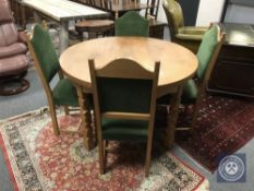 An oak circular extending dining room table and six green upholstered chairs,