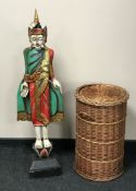 A carved wooden painted figure of an eastern deity together with a circular wicker laundry basket