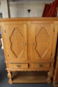 A blonde oak double door cabinet on stand