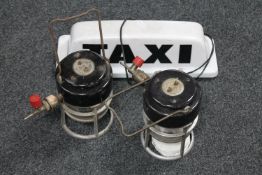 Two gas tilley lamps and an illuminated taxi sign