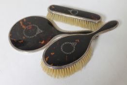 A three piece silver and enamel tortoiseshell backed dressing table brush set
