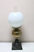 An antique brass oil lamp with glass chimney and shade on cast iron base
