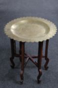 An ornate brass topped table on a folding wooden base