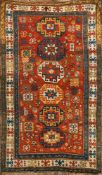 A Kazak rug:, the brick red field with a row of six octagonal and stellar medallions,
