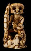 A late 19th century carved walrus tusk netsuke: in the form of a skeleton holding the hand of a