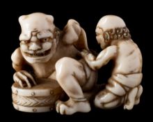A late 19th century carved ivory netsuke: of a horned demon leaning on a drum whilst being attended