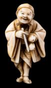 A Japanese carved ivory netsuke of a travelling priest or poet: the smiling man wearing a flowing
