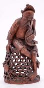 A Chinese bamboo carving of a fisherman: holding a carp and seated on a large basket,