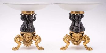 A pair of bronze and gilt bronze tazze: the opaque circular glass dishes mounted on three cherub