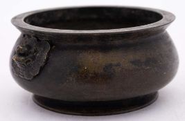A Chinese bronze censer: of squat circular form, with stylized dragon mask handles to the sides,