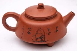 A Chinese Yixing tripod teapot and cover: decorated in black with the seated figure of Hotei,