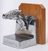 A nickel plated car mascot bookend in the form of the head of a race horse,: on wooden plaque.