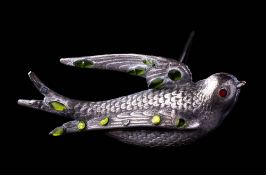 An early 20th century white metal hat pin in the form of a flying bird: set red and green glass,