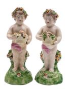 Two Derby figures of putti: each holding a basket of flowers, on green mound bases, patch marks,