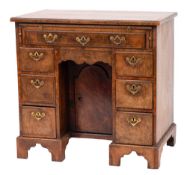 An early 18th Century walnut and feather banded kneehole desk: the wide crossbanded top with a