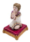 A Bloor Derby figure of a young girl at prayer: kneeling on a gilt and apricot tasselled burgundy