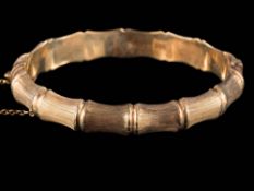 A 9ct gold bamboo-style bangle: with attached safety chain, approximately 16gms gross weight.