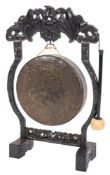 A circular hammered brass gong on a Chinese carved hardwood stand:,