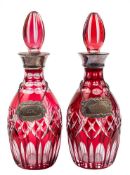 A pair of ruby and clear overlay glass decanters and stoppers: with plated mounts and labels,